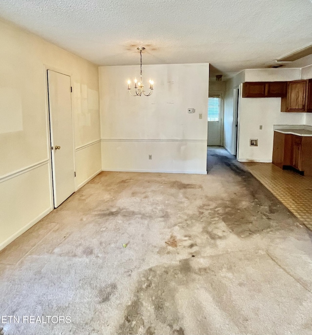 unfurnished dining area with carpet flooring, a textured ceiling, and an inviting chandelier