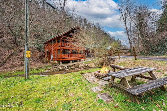 view of yard featuring a deck, a fire pit, and a wooded view