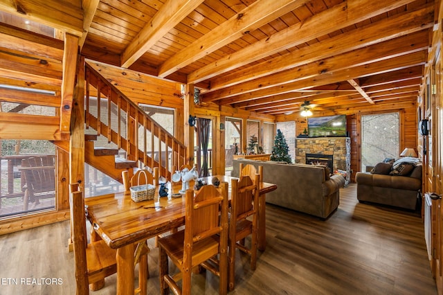 dining room featuring beamed ceiling, stairs, a stone fireplace, wooden ceiling, and wood finished floors