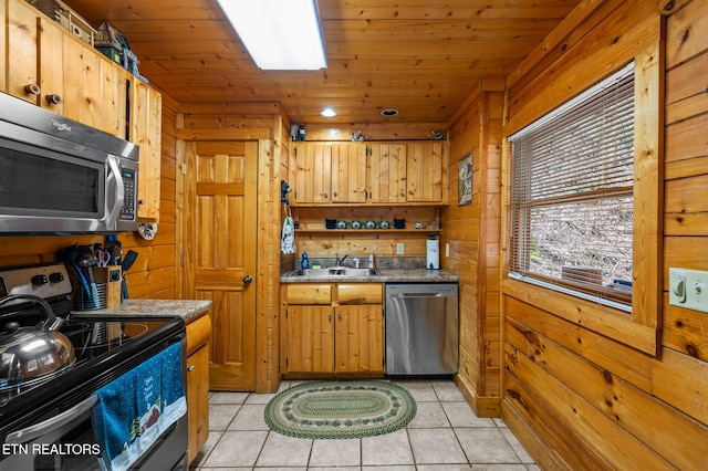 kitchen with light tile patterned floors, a sink, wood walls, appliances with stainless steel finishes, and wooden ceiling