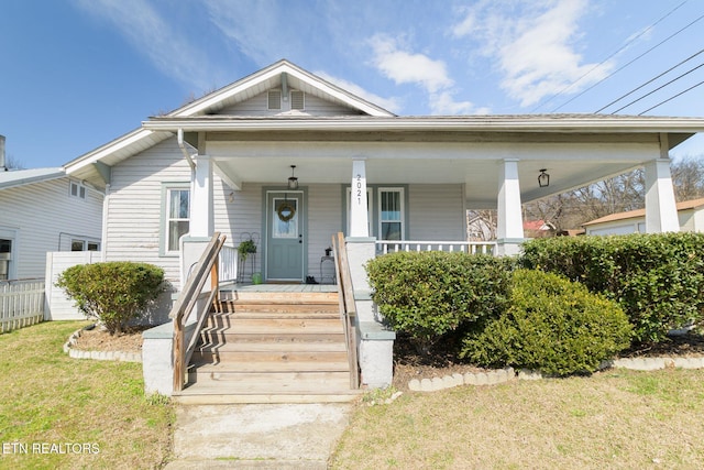 view of front of home with covered porch, a front lawn, and fence