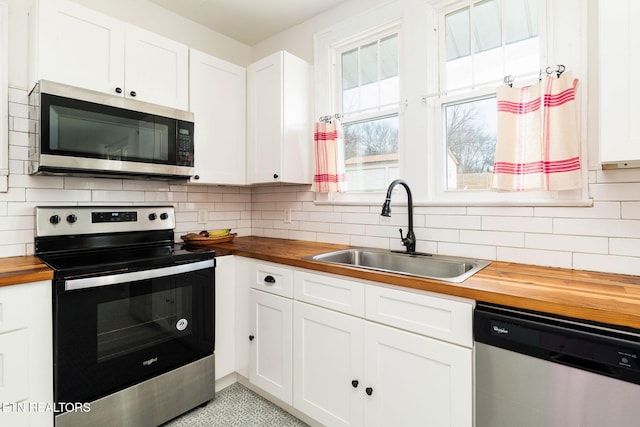 kitchen featuring a sink, decorative backsplash, appliances with stainless steel finishes, and butcher block countertops