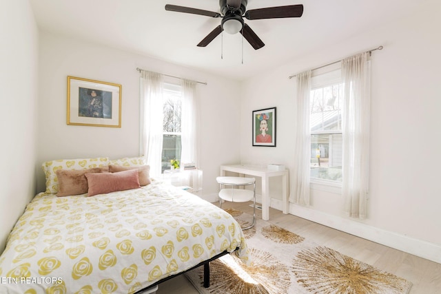 bedroom featuring baseboards, multiple windows, wood finished floors, and a ceiling fan