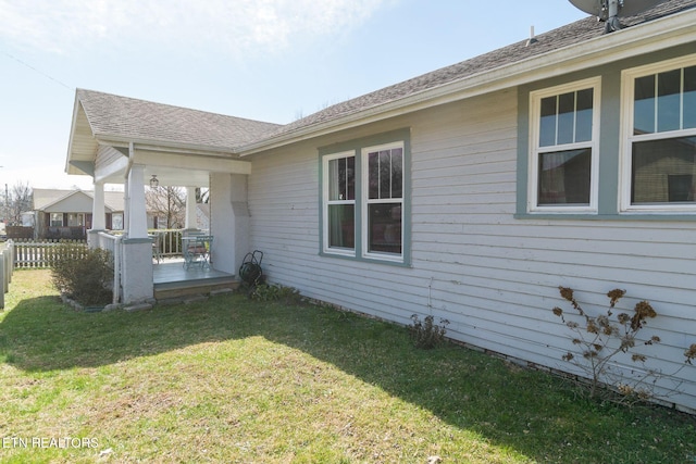 view of side of home with a yard, fence, and a shingled roof