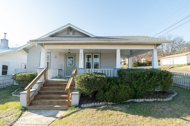 bungalow-style home featuring covered porch, a shingled roof, a front yard, and fence