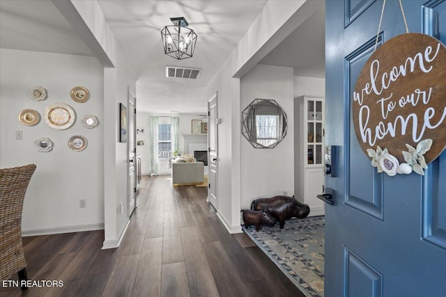 foyer entrance featuring dark wood-style floors, visible vents, baseboards, a fireplace, and a notable chandelier