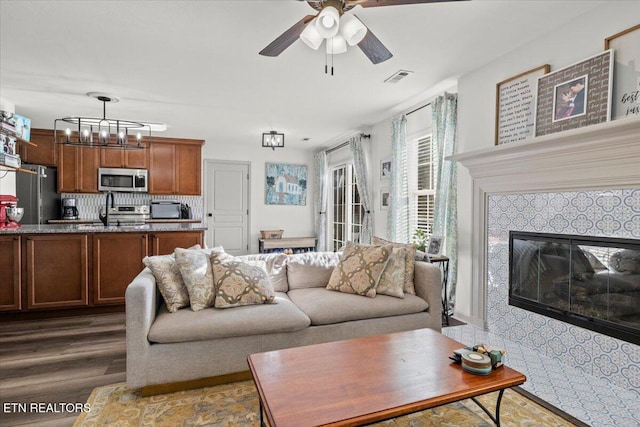 living room with visible vents, ceiling fan with notable chandelier, a tile fireplace, and wood finished floors