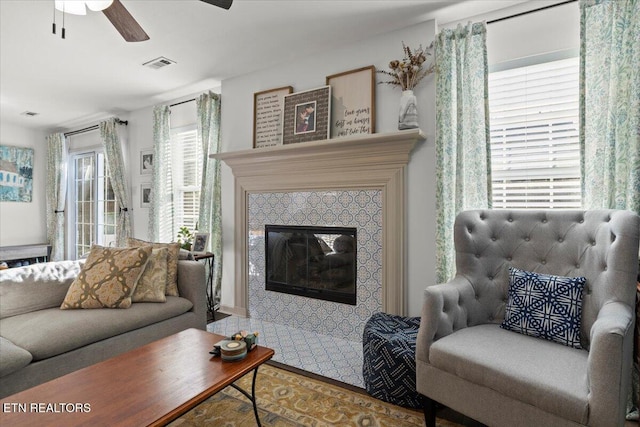 living area with visible vents, a ceiling fan, and a tiled fireplace