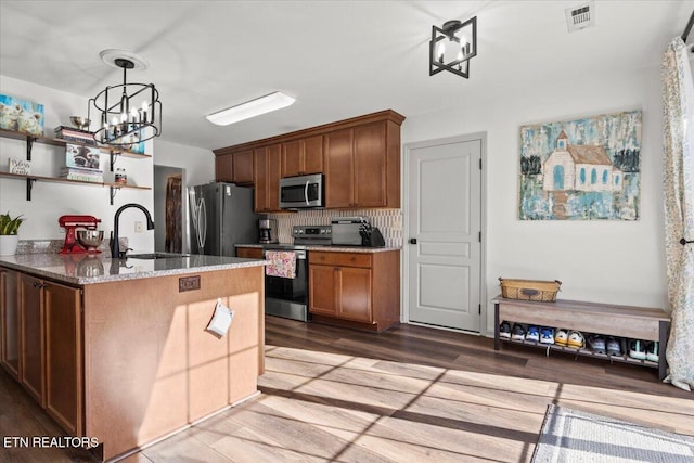 kitchen with visible vents, a sink, light stone counters, stainless steel appliances, and a chandelier