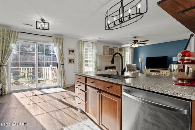 kitchen with brown cabinetry, light wood-style flooring, a fireplace, a sink, and dishwasher