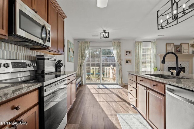 kitchen featuring brown cabinets, a sink, wood finished floors, stainless steel appliances, and light stone countertops