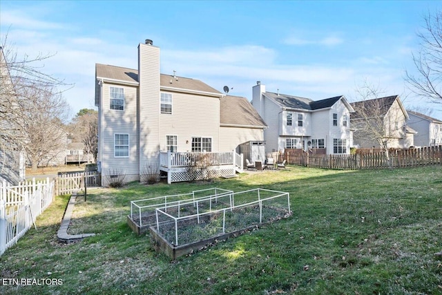 back of house featuring a lawn, a chimney, a fenced backyard, a deck, and a vegetable garden