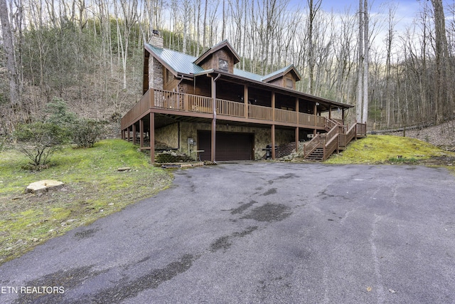 view of front of house featuring a chimney, an attached garage, metal roof, and a view of trees