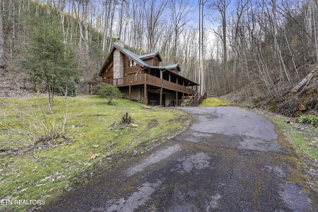 view of side of property featuring driveway, a chimney, a deck, and a view of trees