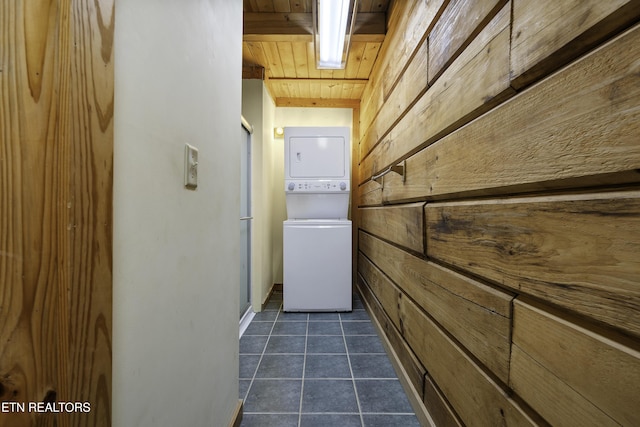 laundry room featuring stacked washer / drying machine, wooden walls, wood ceiling, and dark tile patterned floors