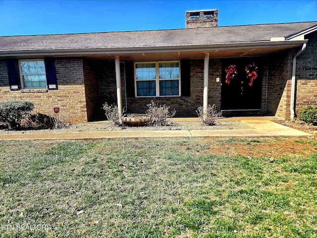 view of front facade featuring brick siding, a chimney, and a front lawn