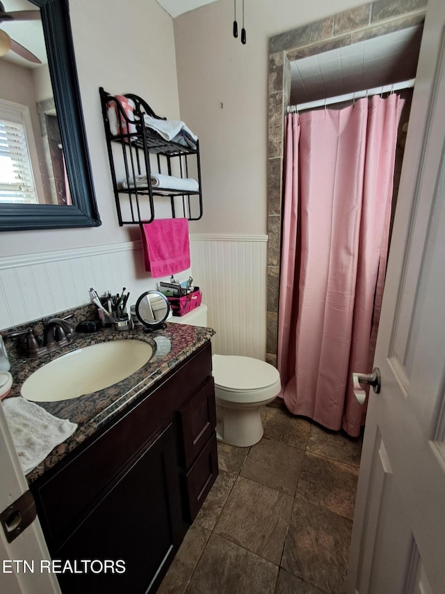 full bathroom featuring vanity, a shower with curtain, ceiling fan, wainscoting, and toilet