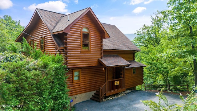 view of front of house with log siding, roof with shingles, and fence