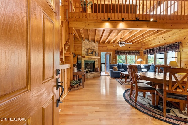 dining room featuring wooden walls, a fireplace, a ceiling fan, and light wood-style floors