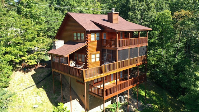 back of house featuring roof with shingles, log siding, a chimney, a balcony, and a sunroom