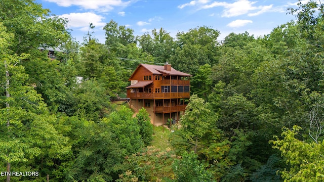 rear view of property with a wooden deck, a wooded view, and a chimney