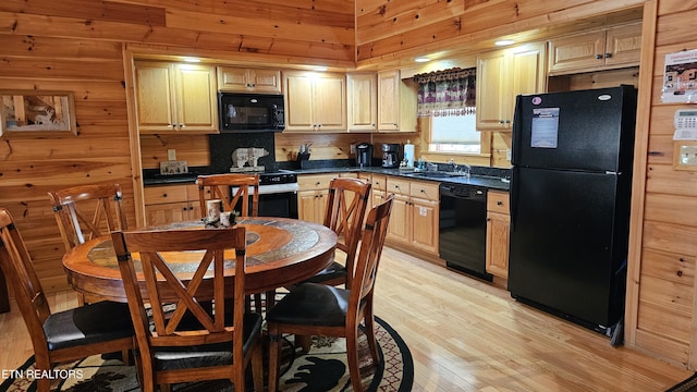 kitchen with dark countertops, wood walls, light wood-type flooring, black appliances, and a sink