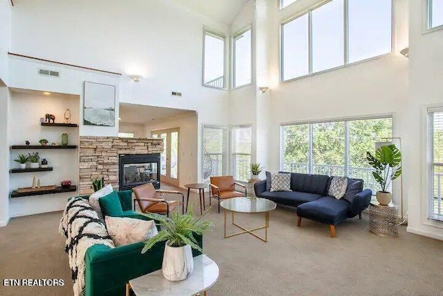 living area featuring a wealth of natural light, visible vents, carpet floors, and a stone fireplace