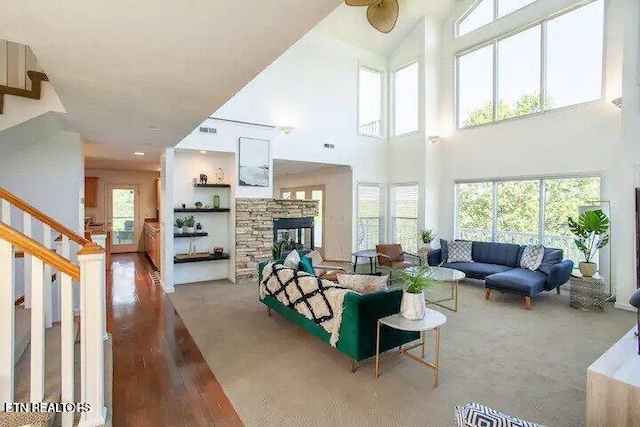 living area with wood finished floors, visible vents, a high ceiling, a fireplace, and stairs