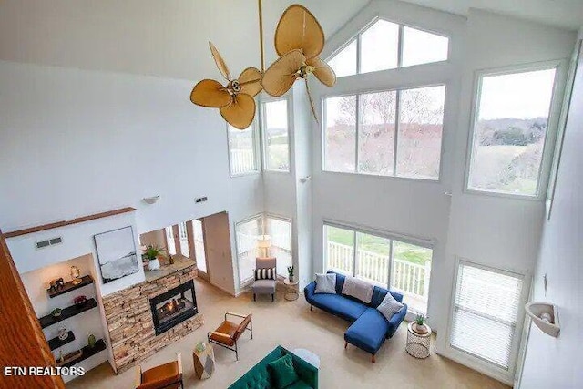 living room featuring a stone fireplace, ceiling fan, visible vents, and high vaulted ceiling