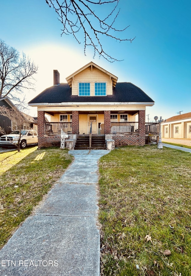 bungalow-style home with brick siding, a porch, a chimney, and a front yard