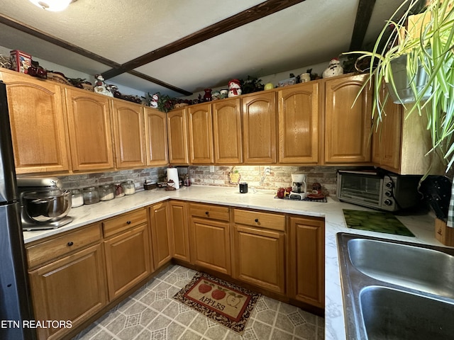 kitchen with a toaster, light countertops, decorative backsplash, a textured ceiling, and a sink