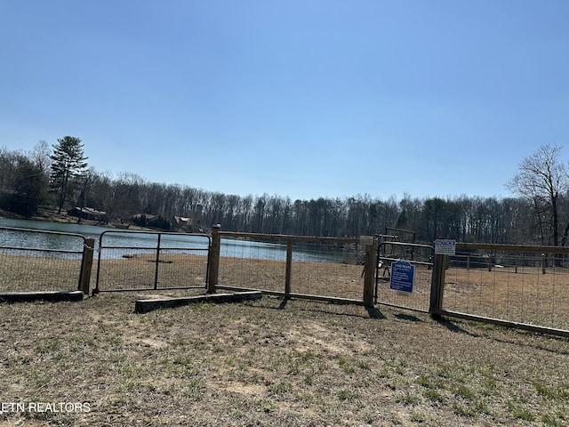 view of yard with a wooded view, a gate, fence, and a water view