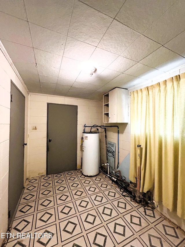 basement featuring concrete block wall, light floors, and water heater