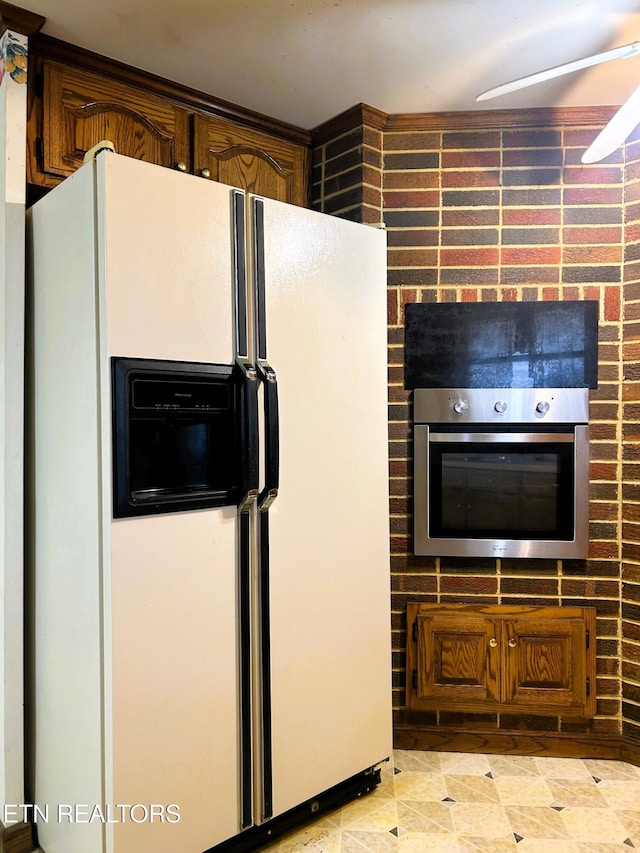 kitchen featuring stainless steel oven, brown cabinets, and white fridge with ice dispenser