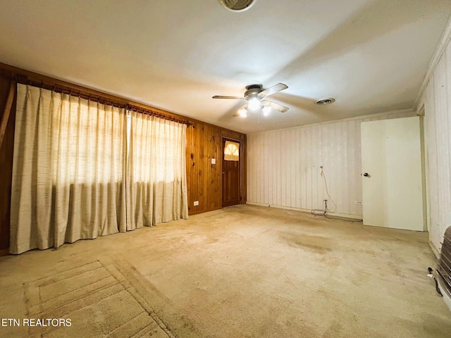 unfurnished living room featuring wooden walls, visible vents, carpet flooring, and a ceiling fan