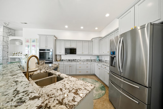 kitchen with a sink, stainless steel appliances, light stone counters, and light tile patterned floors