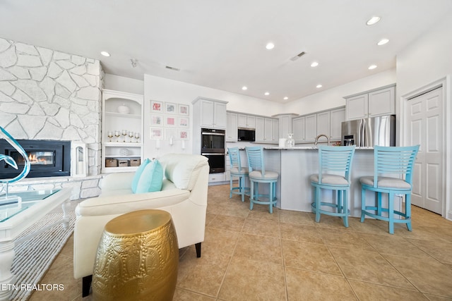 kitchen featuring a breakfast bar area, light tile patterned floors, a fireplace, stainless steel fridge, and open floor plan