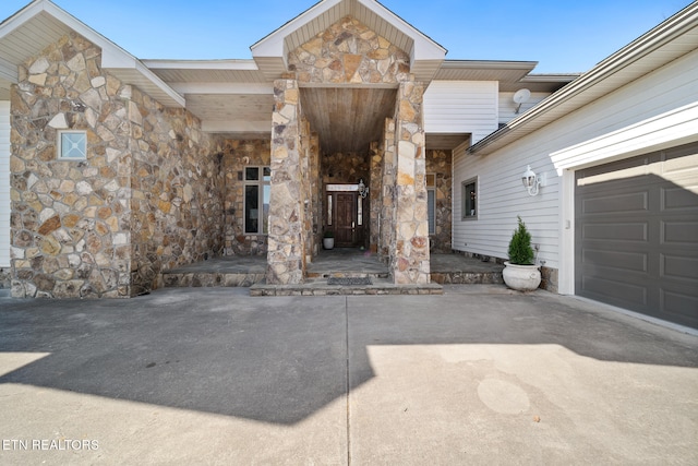 view of exterior entry featuring an attached garage, stone siding, and driveway