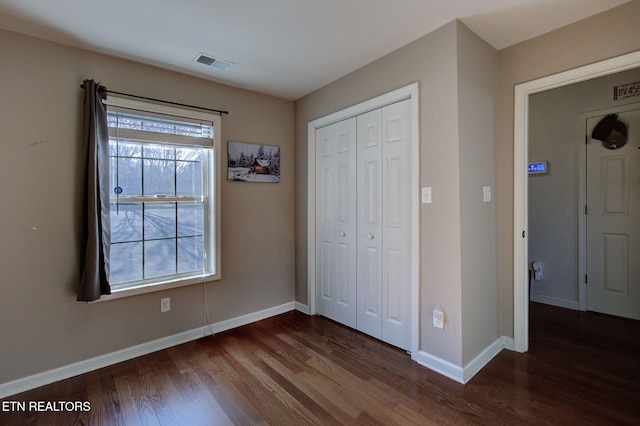 unfurnished bedroom with a closet, baseboards, visible vents, and dark wood-style flooring