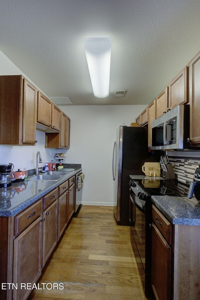 kitchen with dark countertops, visible vents, light wood-style flooring, stainless steel appliances, and a sink