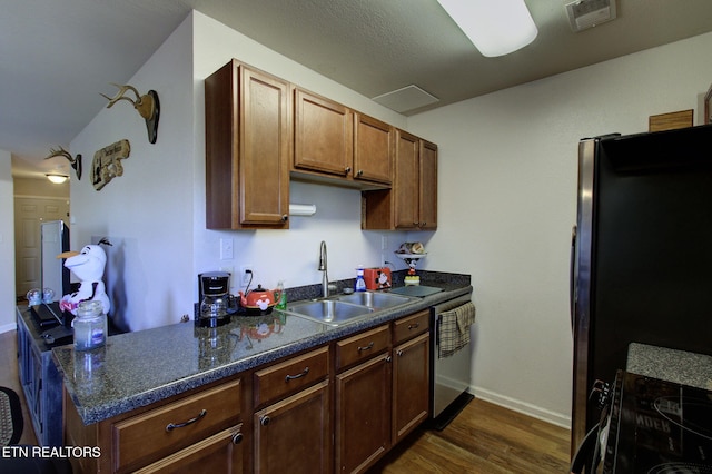 kitchen with visible vents, a sink, dishwasher, freestanding refrigerator, and dark wood-style flooring