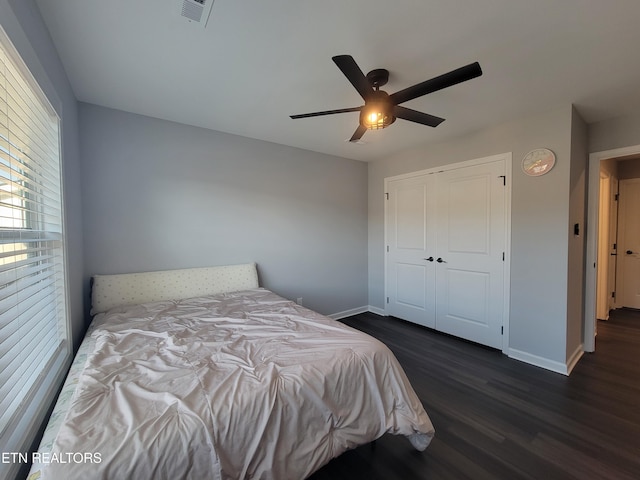 bedroom featuring dark wood-style floors, visible vents, baseboards, ceiling fan, and a closet