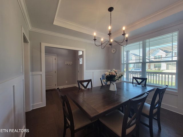 dining room featuring an inviting chandelier, a tray ceiling, dark wood-style flooring, ornamental molding, and a decorative wall