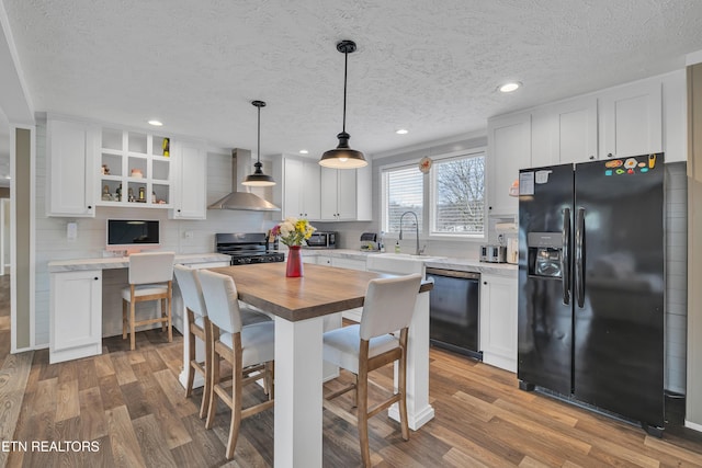 kitchen featuring stainless steel electric range oven, wood counters, dishwasher, wall chimney range hood, and black refrigerator with ice dispenser