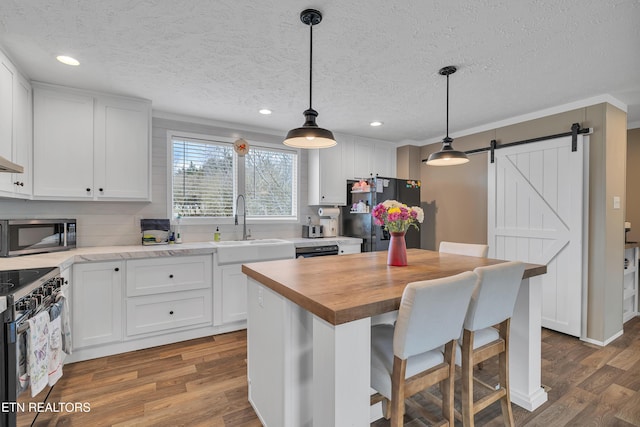 kitchen with stainless steel microwave, a barn door, freestanding refrigerator, white cabinets, and a sink