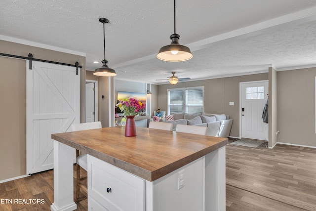 kitchen with wood finished floors, wooden counters, a textured ceiling, white cabinetry, and a barn door