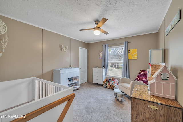 bedroom with ceiling fan, ornamental molding, carpet floors, a textured ceiling, and a nursery area