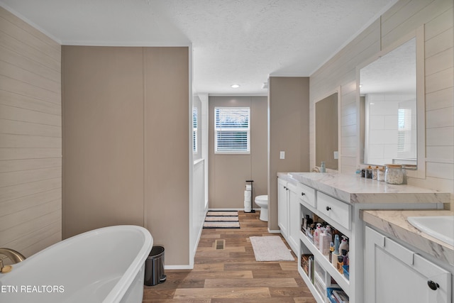 bathroom with double vanity, a freestanding tub, toilet, and wood finished floors