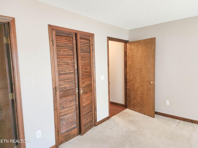 unfurnished bedroom featuring a closet, a textured ceiling, carpet, and baseboards