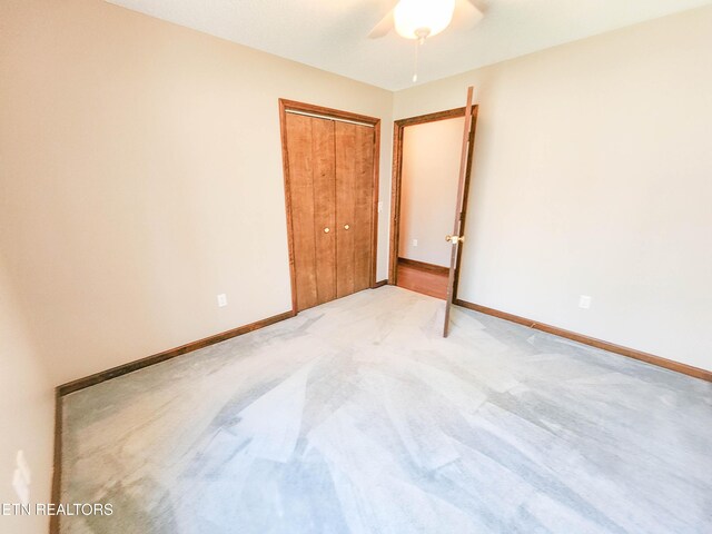 unfurnished bedroom with a closet, ceiling fan, light colored carpet, and baseboards